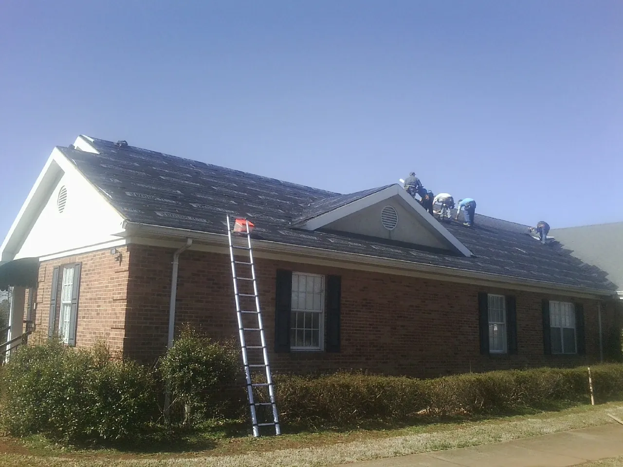 Crew tearing shingles off a brick ranch roof with a ladder set — Emergency Roof Repair work by our crew in Greenback