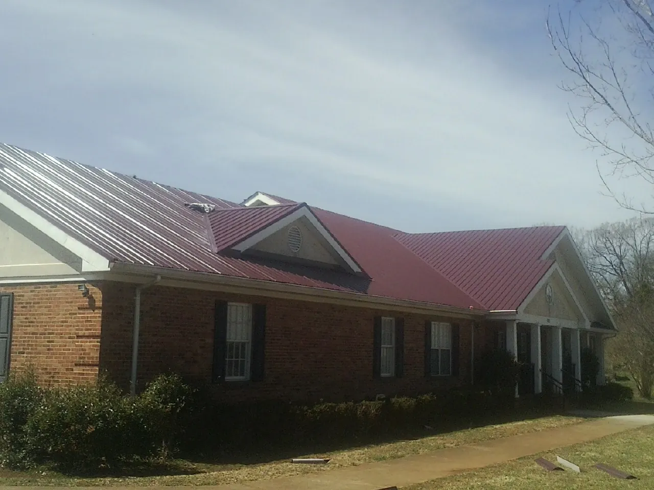 Red metal roof with gabled entries on a long brick building, from a Hail Damage Roof Repair job in Greenback